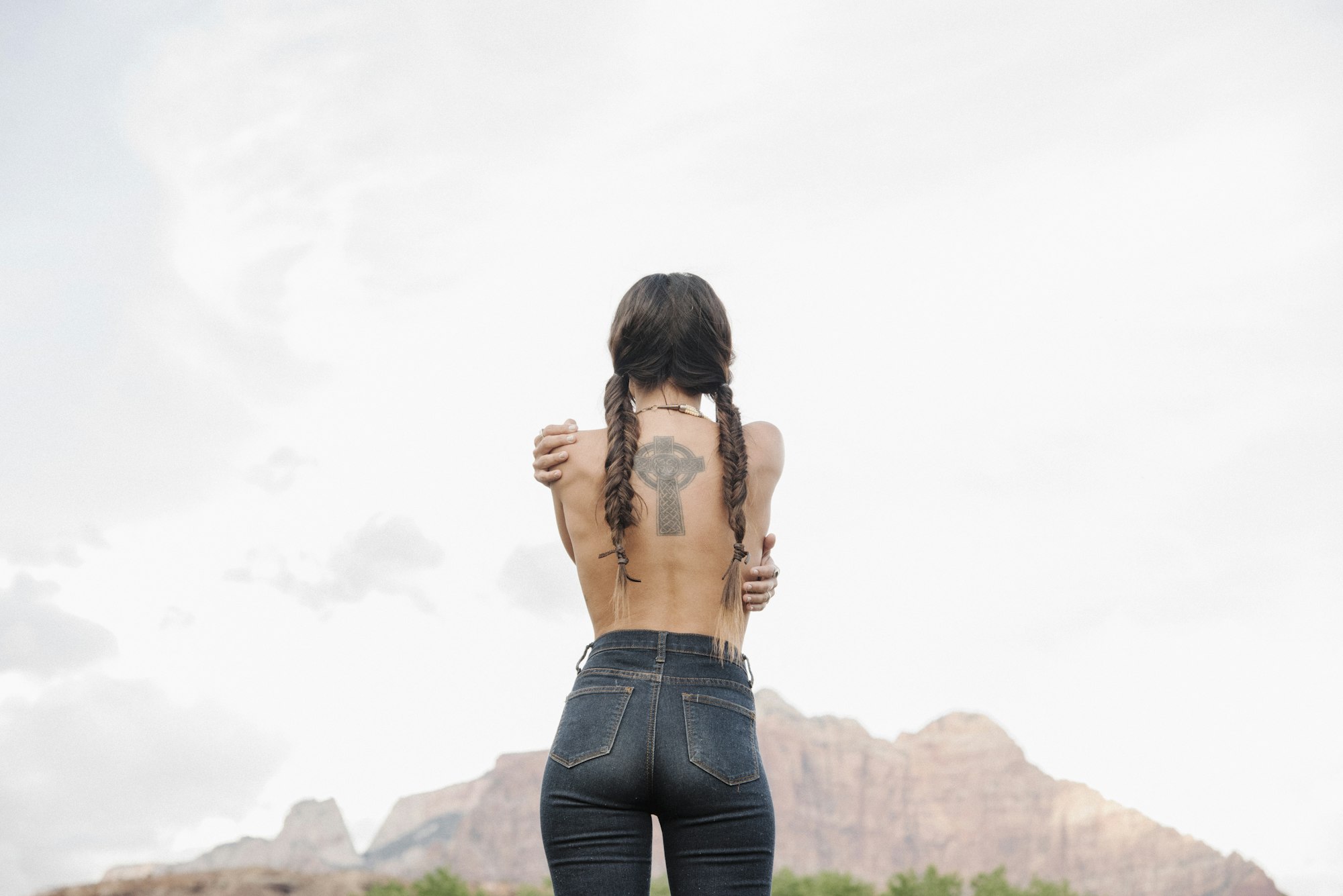 Rear view of Topless young woman wearing jeans, tattoo of a Celtic Cross